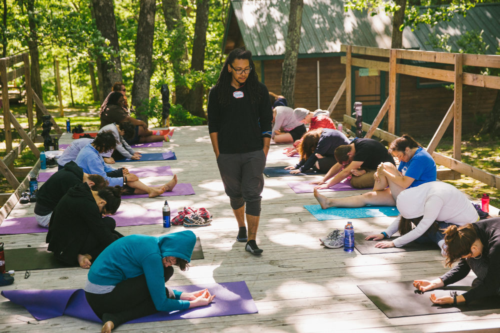 Counselor at Camp Bonfire, adult summer camp, leads a group through a yoga class.
